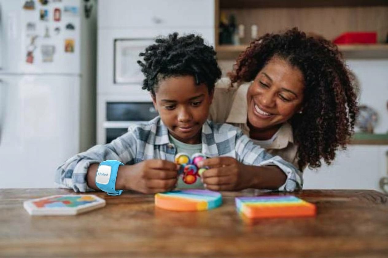 Maman souriante avec son fils qui porte la montre KiddoWatch, jouant à table